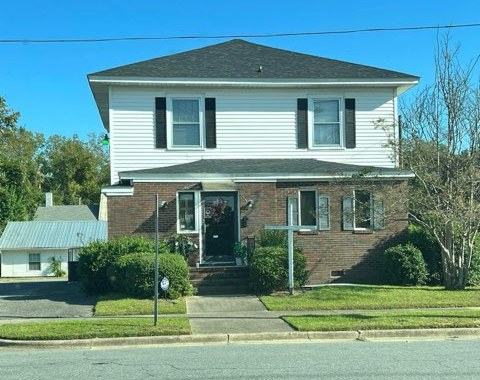 The church: a two-story house with white siding, black shutters and a brick front porch, with a white cross out front